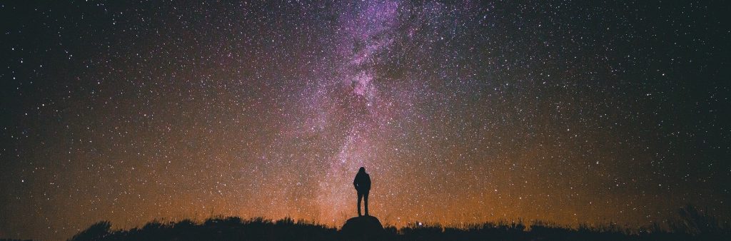 Silhouette of woman looking above & beyond to the night sky.